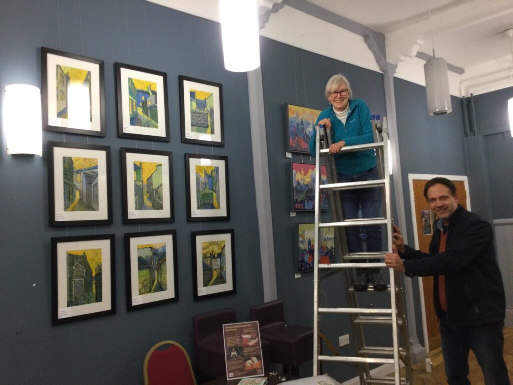 Foyer of Biggar Corn Exchange for Biggar Little Festival 2024 with Ronnie Cruwys up on ladder, and musician Rob Hall on right.